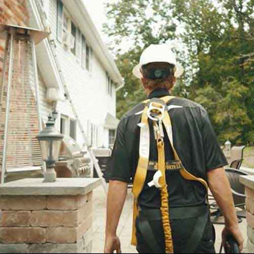Many in full safety equipment white house with long ladder. He is doing real estate inspection.