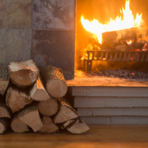 a small pile of wood stacked by a burning fireplace