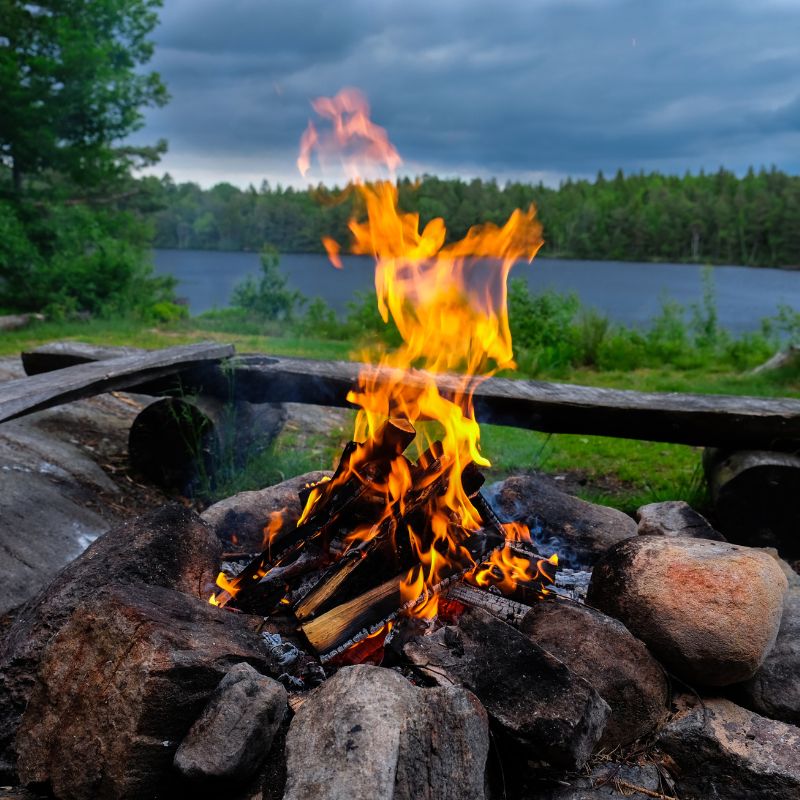 an outside fire surrounding by stones with a lake in the background
